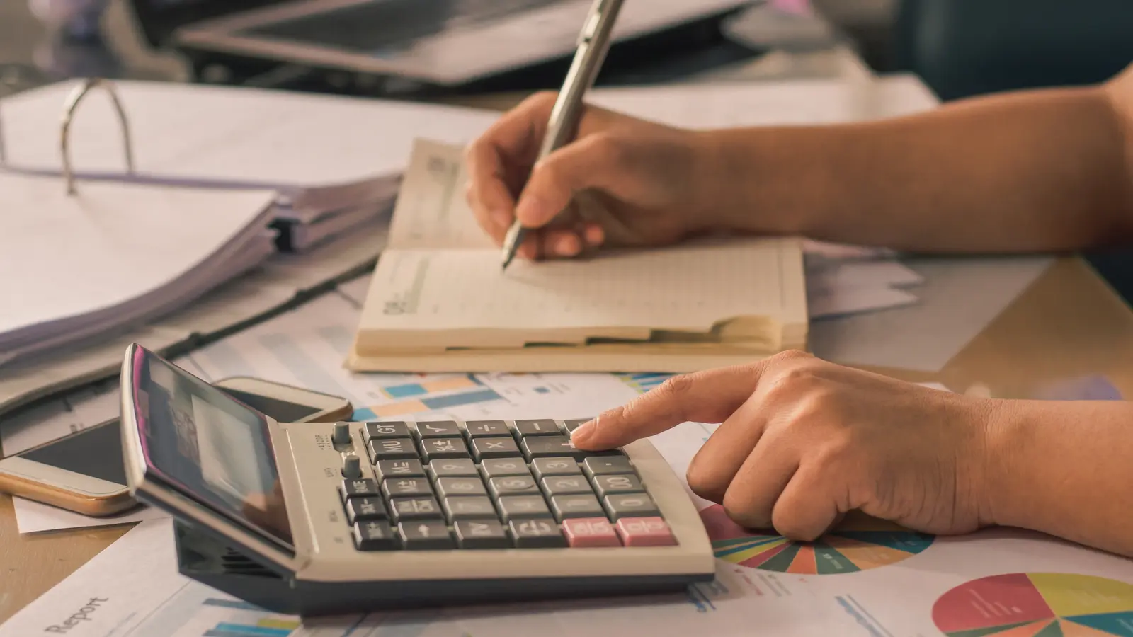 Mains utilisant une calculatrice et prenant des notes dans un carnet, entourées de classeurs