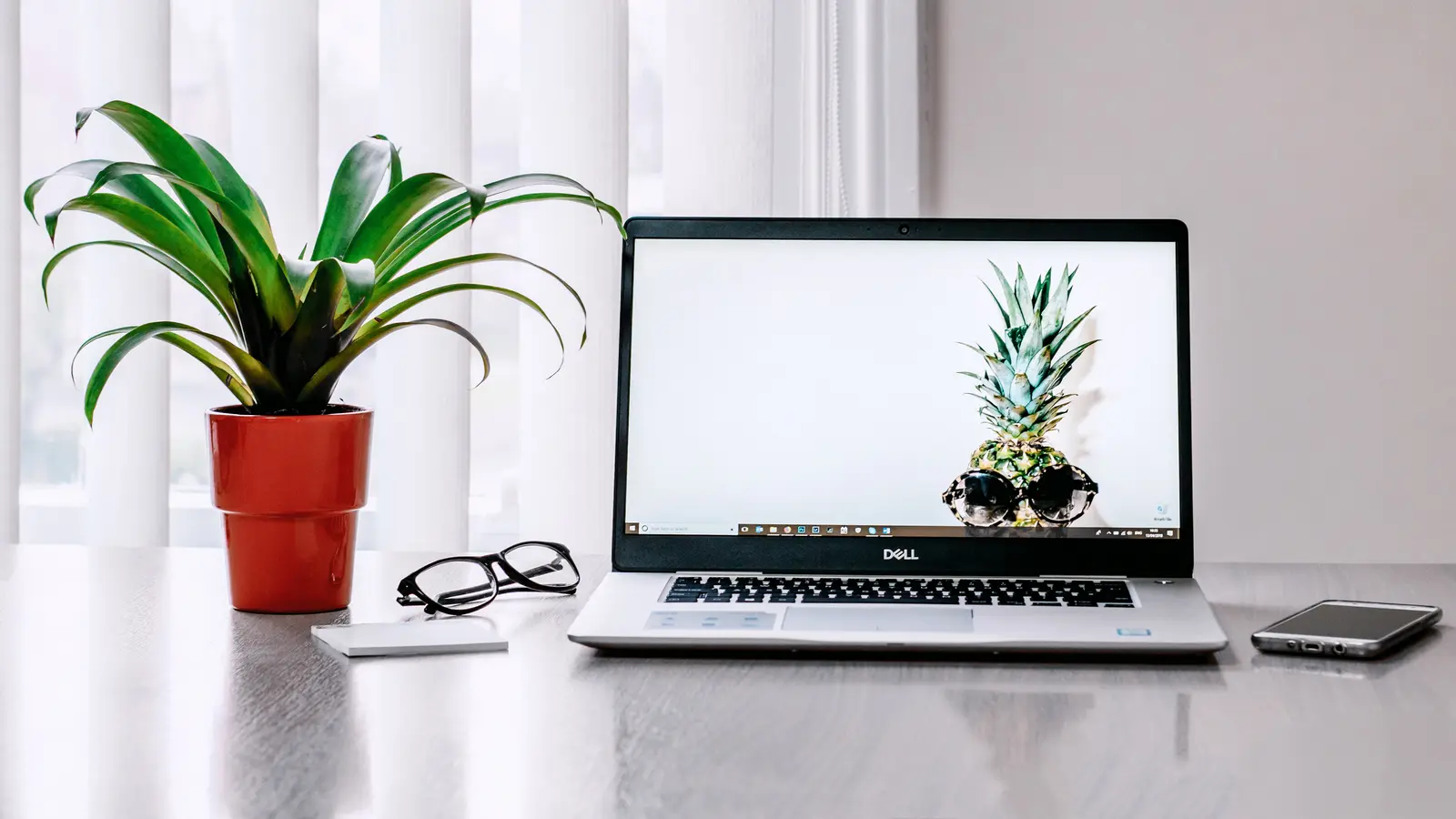 Ordinateur portable sur un bureau blanc, à côté d'une plante verte et d'une paire de lunettes