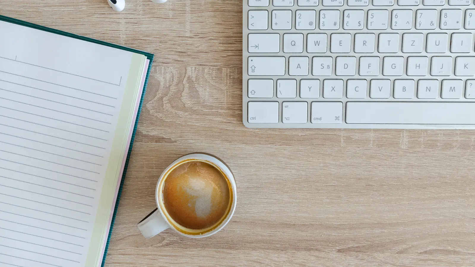 Cahier, clavier et tasse de café sur un bureau en bois, vus de dessus