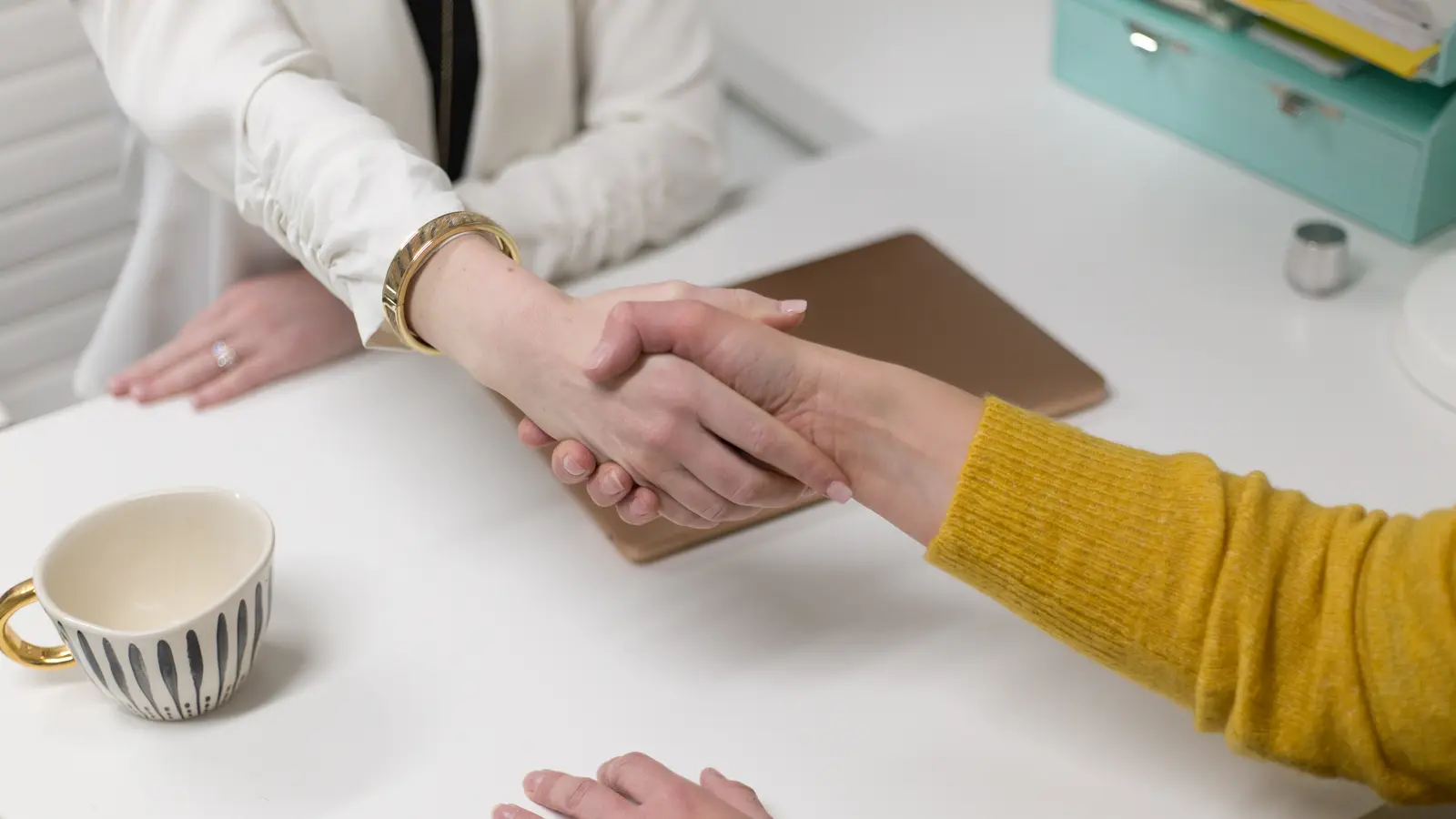 Poignée de main entre deux personnes au-dessus d'une table, à côté d'une tasse de café