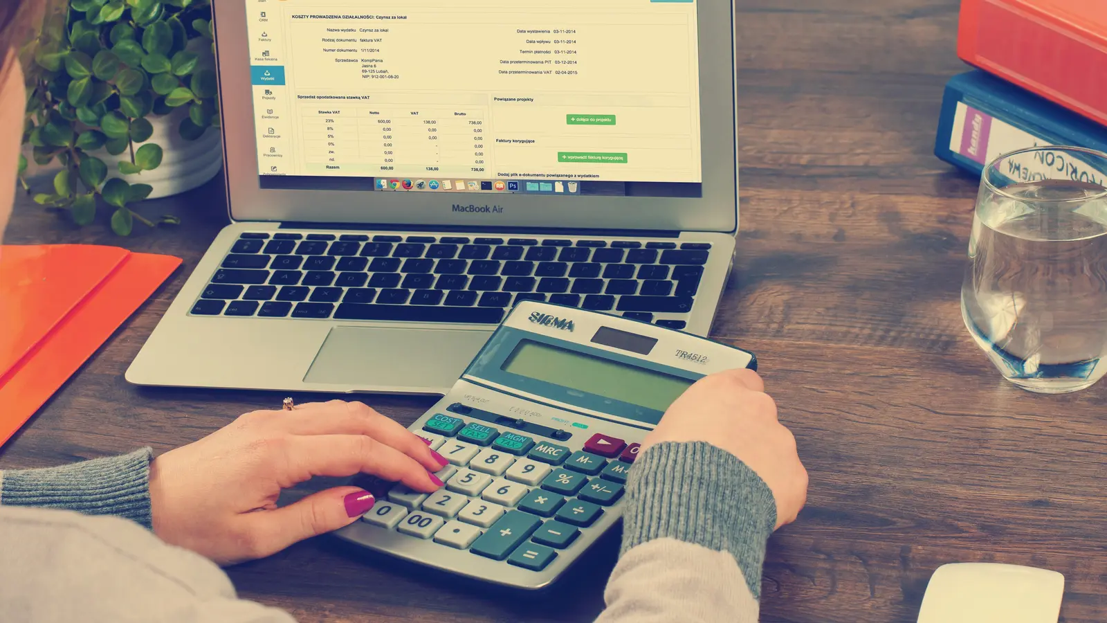 Personne tapant sur une calculatrice devant un ordinateur portable ouvert sur un tableau