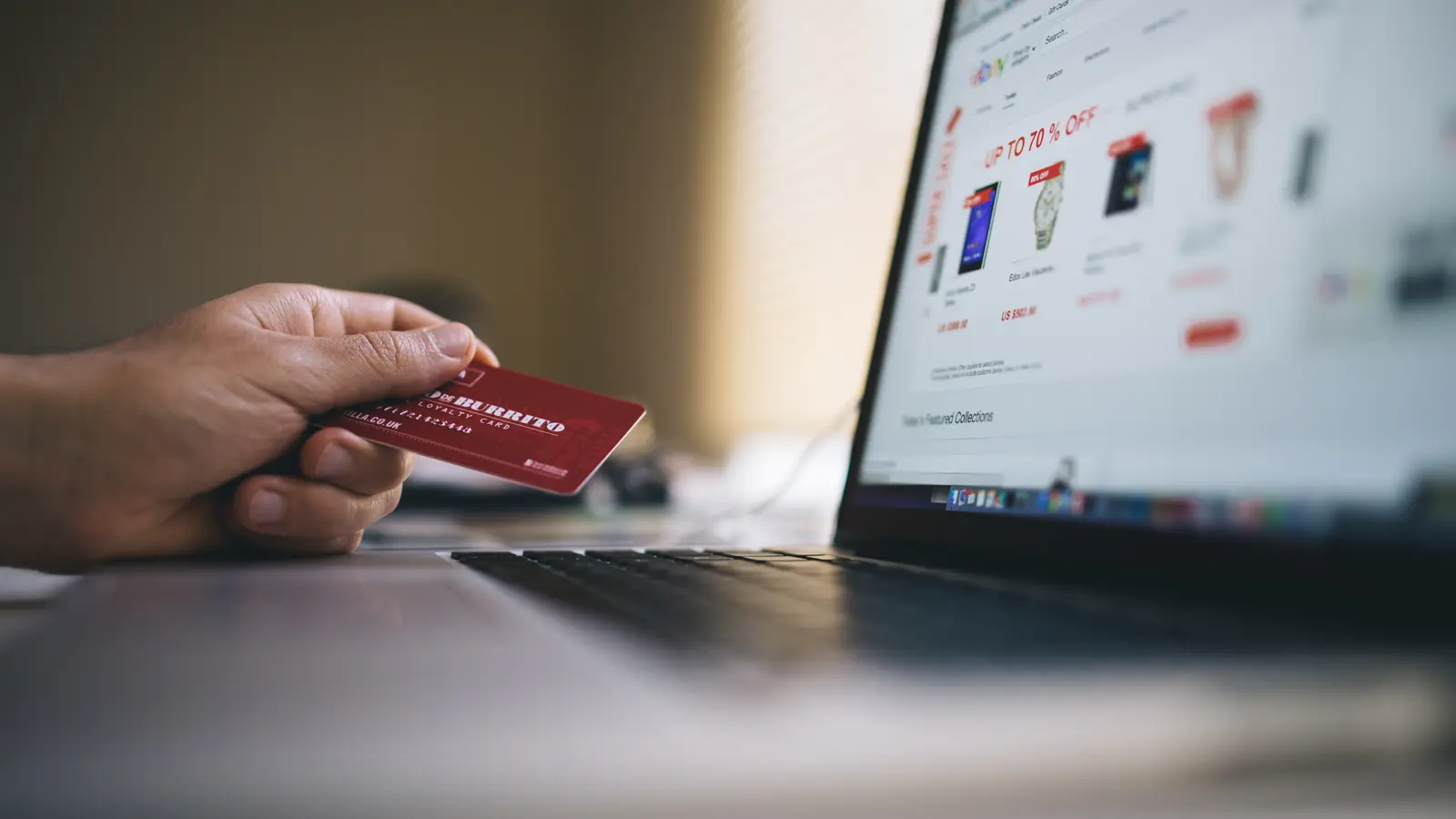 Main tenant une carte bancaire devant un ordinateur portable ouvert sur un site marchand