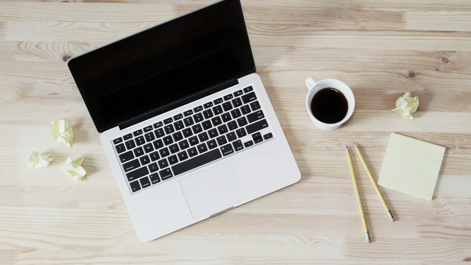 Ordinateur portable, tasse de café, crayons et pense-bête sur un bureau en bois clair