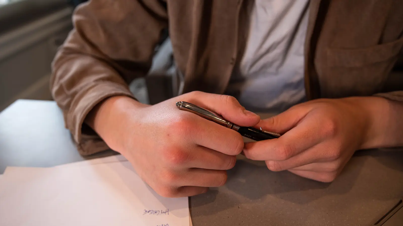 Mains d'un homme tenant un stylo au-dessus d'une feuille posée sur un bureau