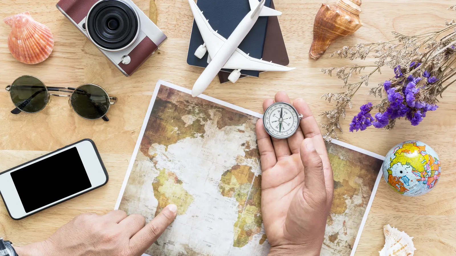 Carte du monde, boussole, téléphone, lunettes de soleil et appareil photo étalés sur une table