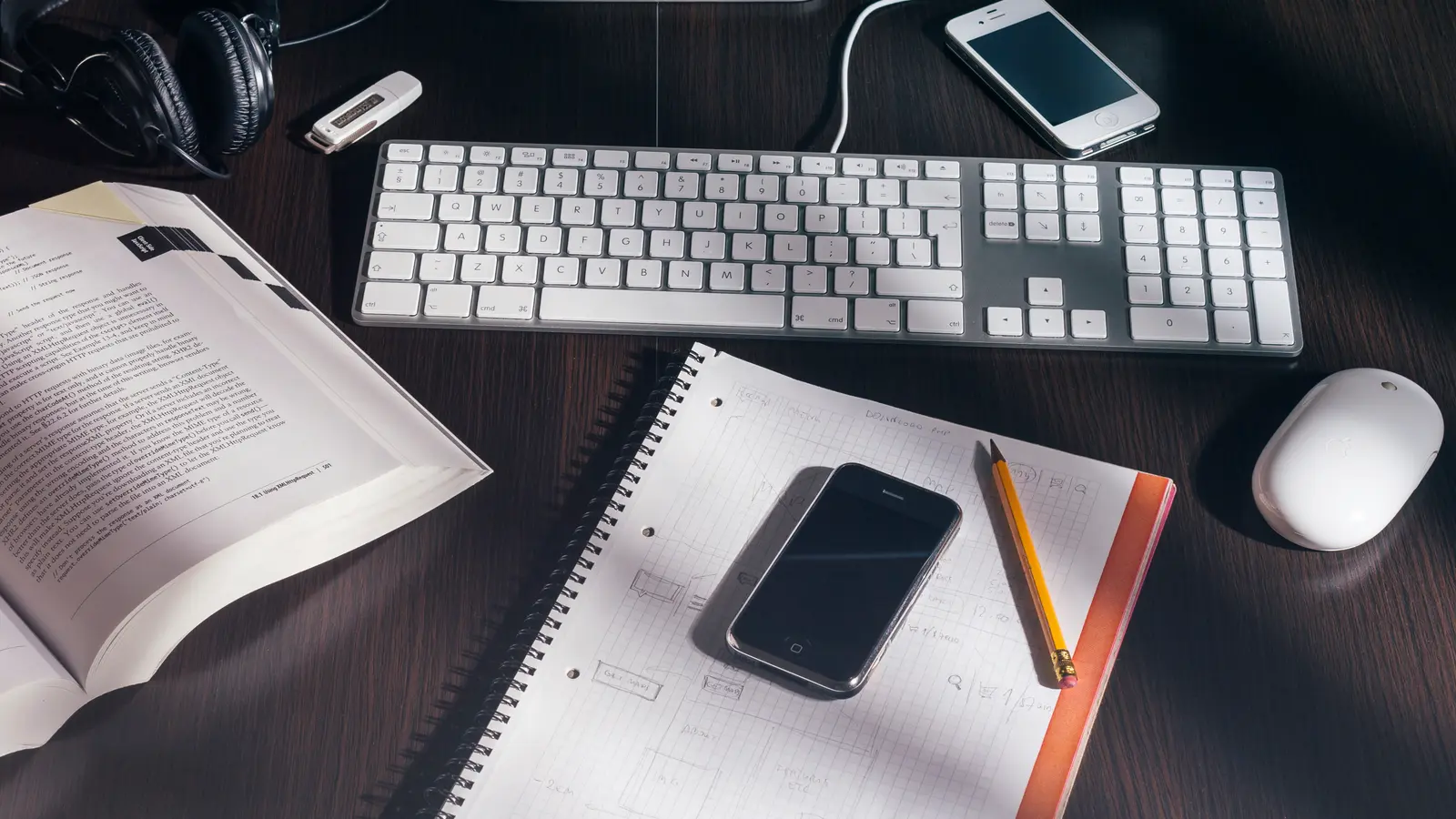 Clavier, cahier, téléphone et livre ouvert sur un bureau sombre, vus de dessus