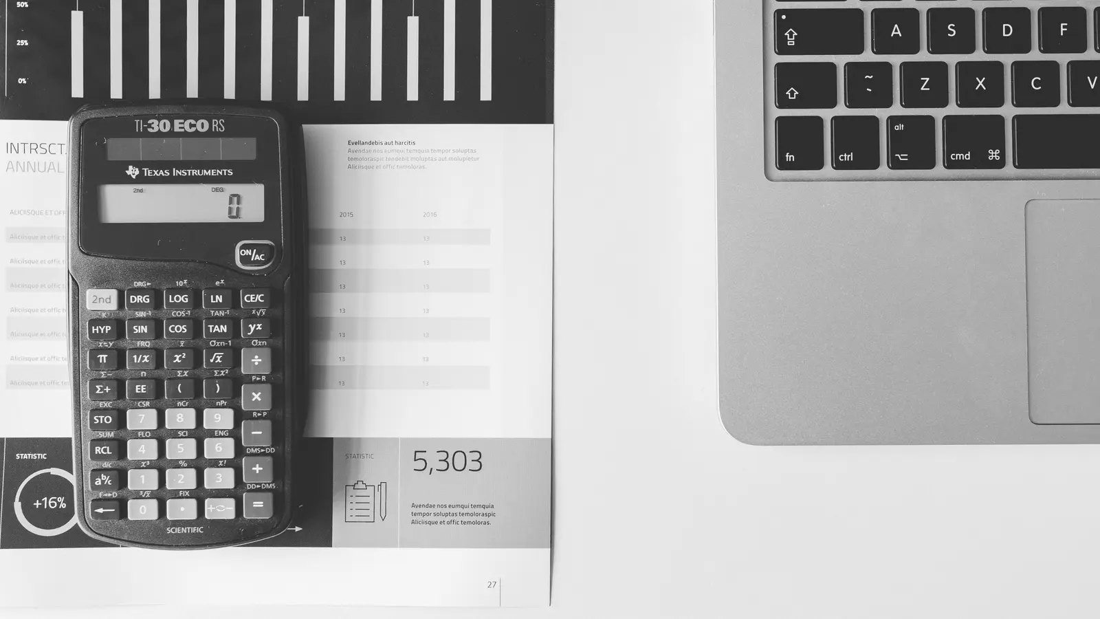 Calculatrice posée sur un rapport chiffré, à côté d'un ordinateur portable