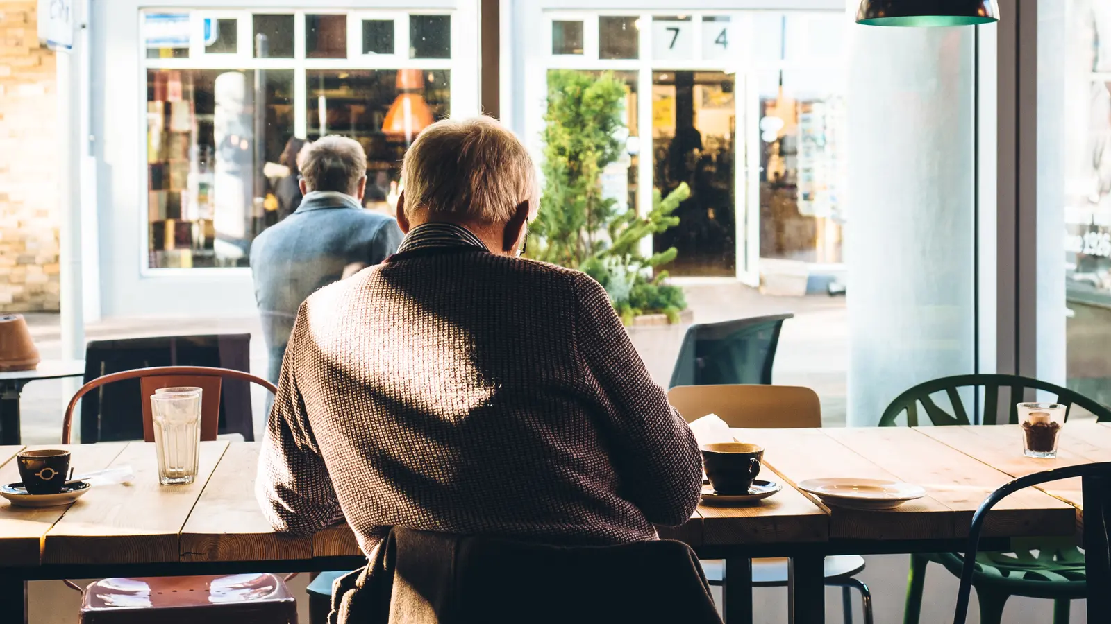 Client âgé assis seul à une table, de dos, dans un café lumineux