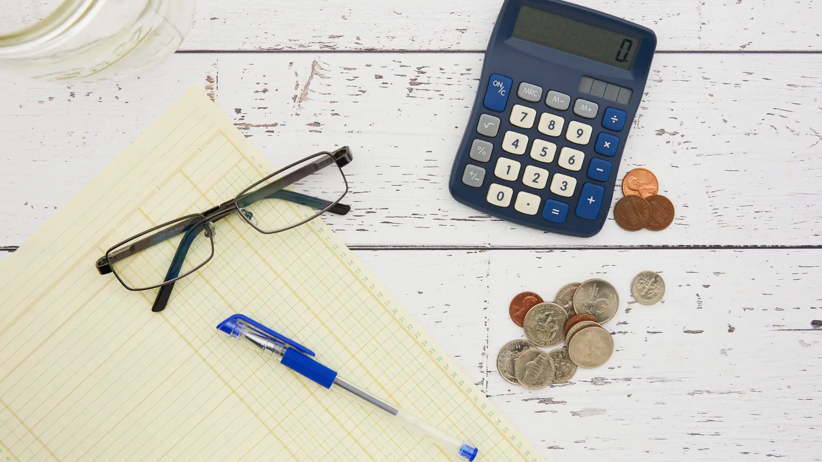 Calculatrice, lunettes, stylo et pièces de monnaie sur un bloc-notes jaune