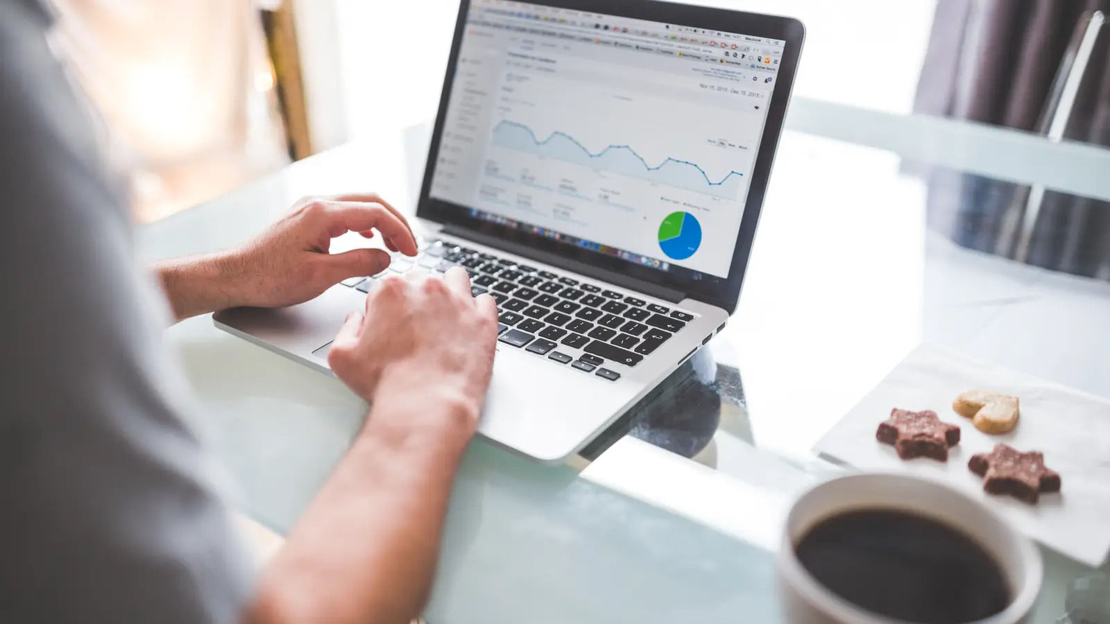 Personne consultant des courbes et un graphique sur un ordinateur portable, à côté d'une tasse de café